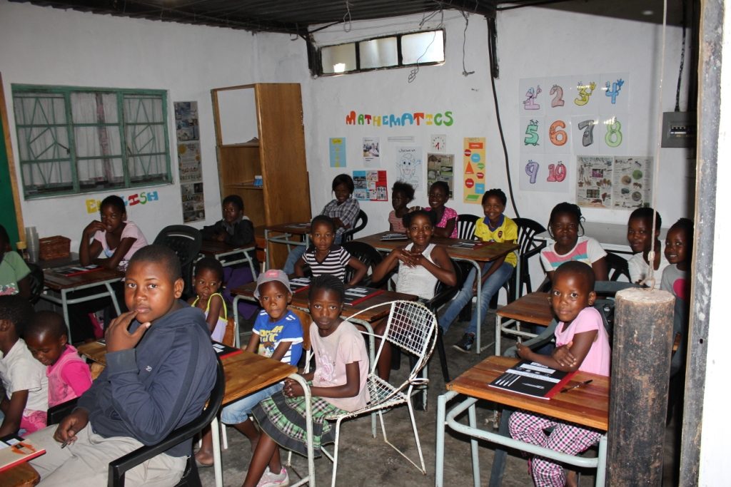 Children seated at desks in Pine View School's first classroom, walls decorated with mathematics and English posters